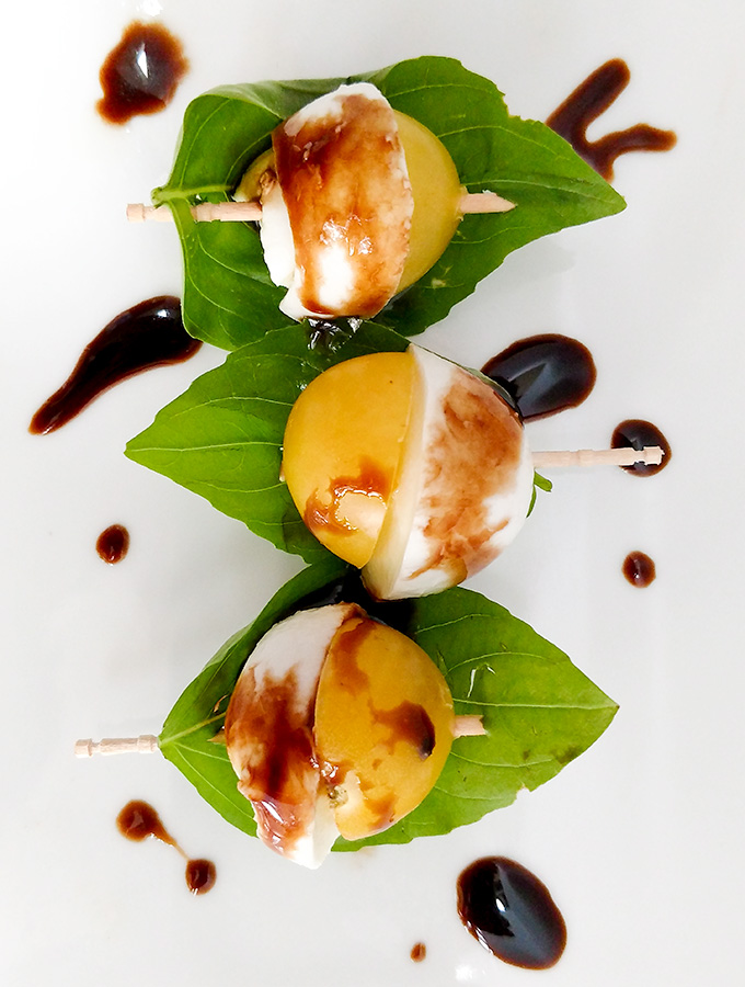 Caprese salad on a toothpick with yellow tomaotes and balsamic vinegar