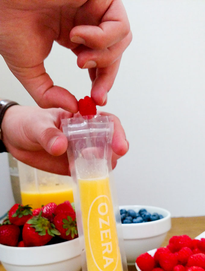 Mango berry popsicle being filled with fresh raspberries, blueberries and strawberries
