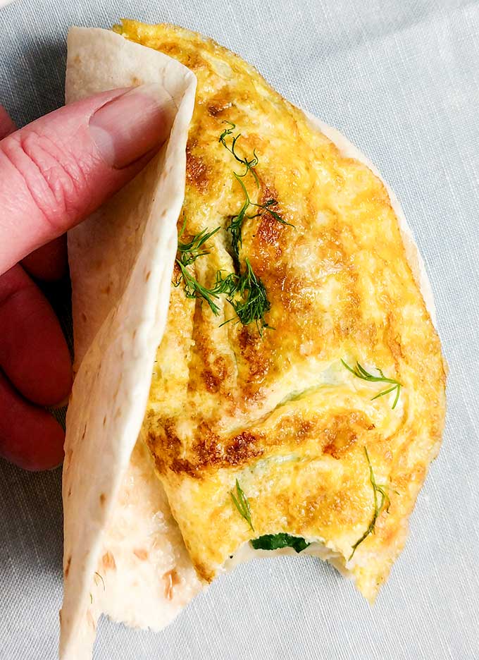 Placing omelette in tortilla for a walking breakfast taco