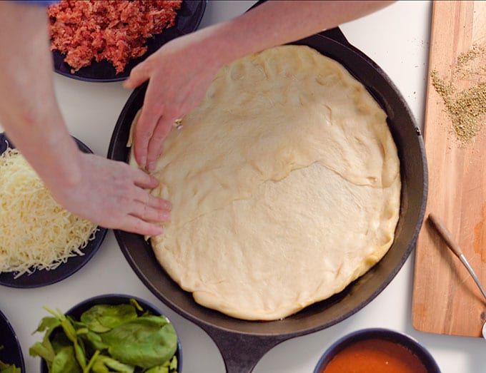 pressing dough in cast iron pan for deep dish pizza